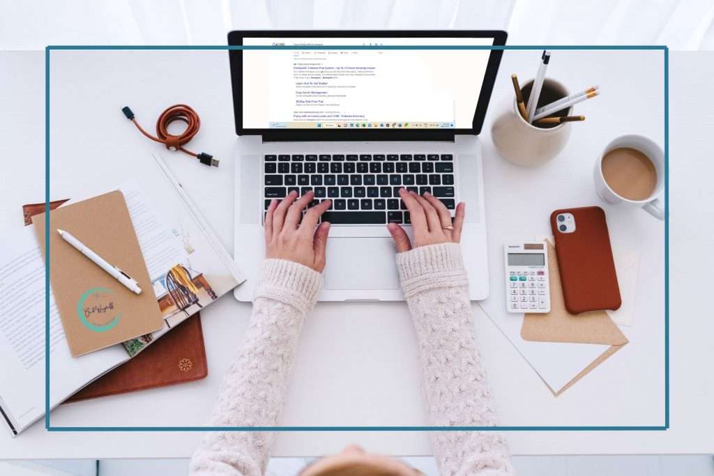woman's hands on laptop. Laptop screen showing a Google SERP. pens, calculator, and notebook on the desk