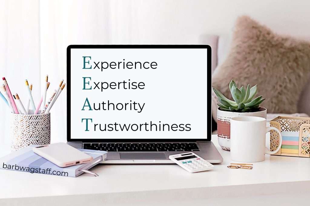 Experience, Expertise, Authority, Trustworthiness written on a computer screen. Notebook, calculator, plant and mug are beside it.