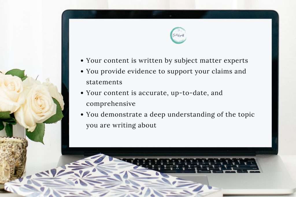 White roses in a gold vase on a table with a blue and white notebook and laptop open to a screen reading "• Your content is written by subject matter experts • You provide evidence to support your claims and statements • Your content is accurate, up-to-date, and comprehensive • You demonstrate a deep understanding of the topic you are writing about"