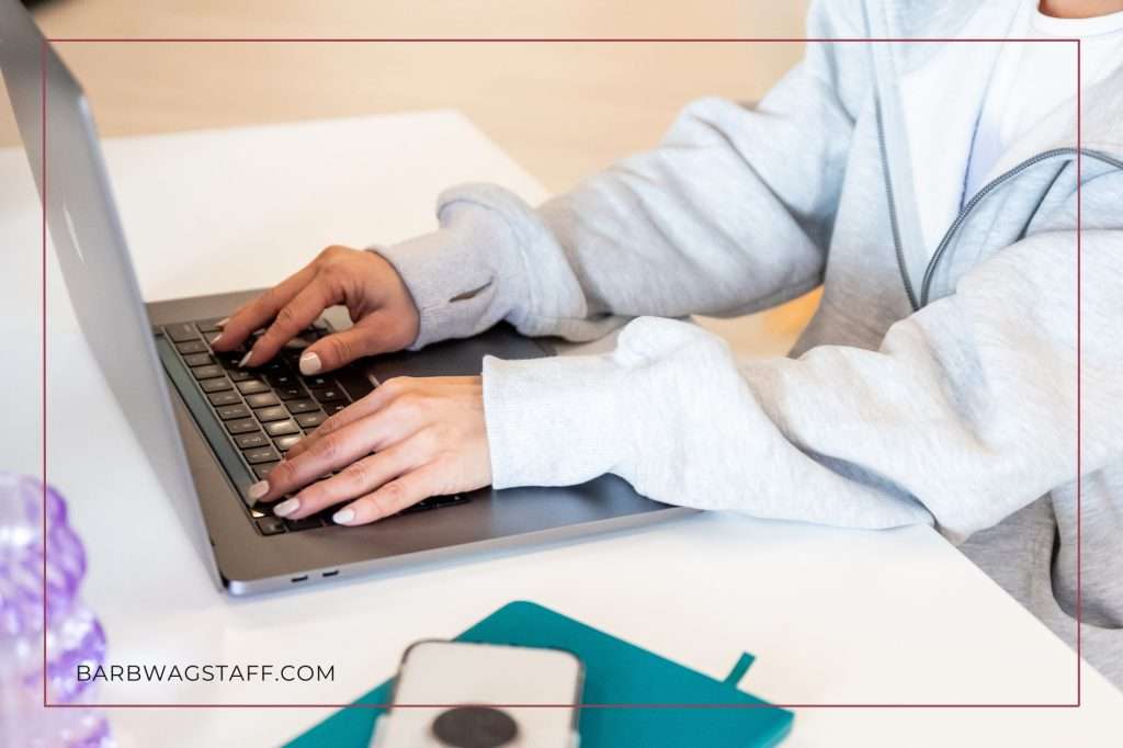 woman in pink shirt with arms in the air looking at her computer screen