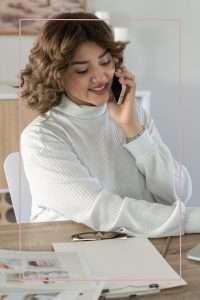 dark-haired woman in white sweater talking on her cellphone while sitting at her desk